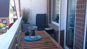 A wooden table with a glass container and a chair on a balcony with a white ceiling and brick walls. - **** classified comfort vacation apartment 300 m to the beach, incl. beach chair  (Grömitz)