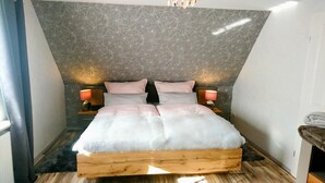 A bedroom with a sloped ceiling, a wooden bed frame, two bedside lamps, and a patterned wall. - **** classified comfort vacation apartment 300 m to the beach, incl. beach chair  (Grömitz)