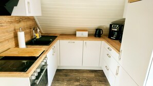 A compact kitchen with white cabinets, a wooden countertop, a black sink, a coffee maker, and a box of bread. - **** classified comfort vacation apartment 300 m to the beach, incl. beach chair  (Grömitz)