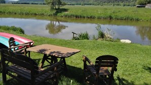 Un montaje para picnic con una mesa y sillas frente a un lago tranquilo, rodeado de exuberante vegetación y colinas al fondo.