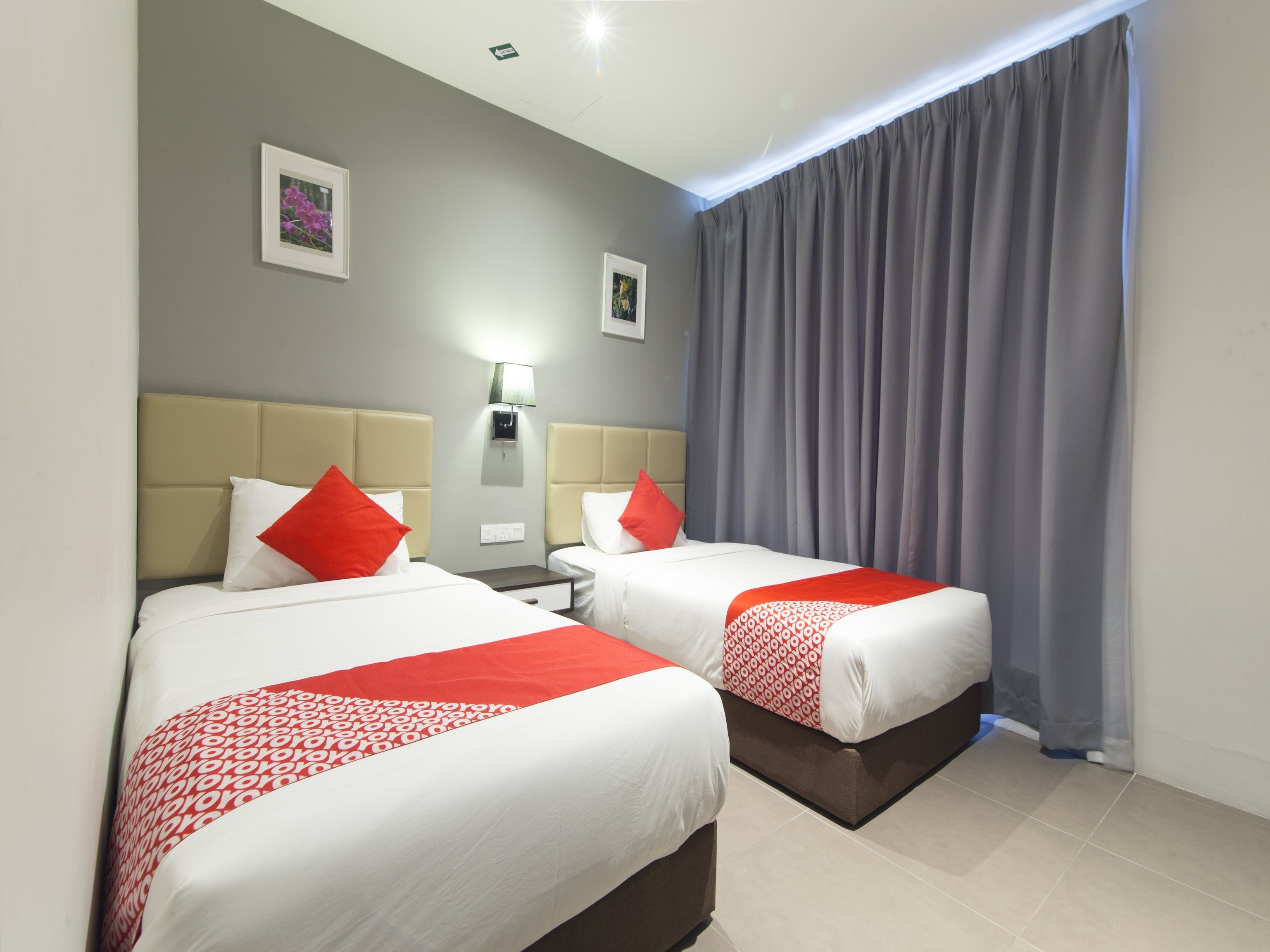 Habitación de hotel con dos camas, cada una con cabecera, mesita de noche y lámpara, además de una ventana con cortinas.