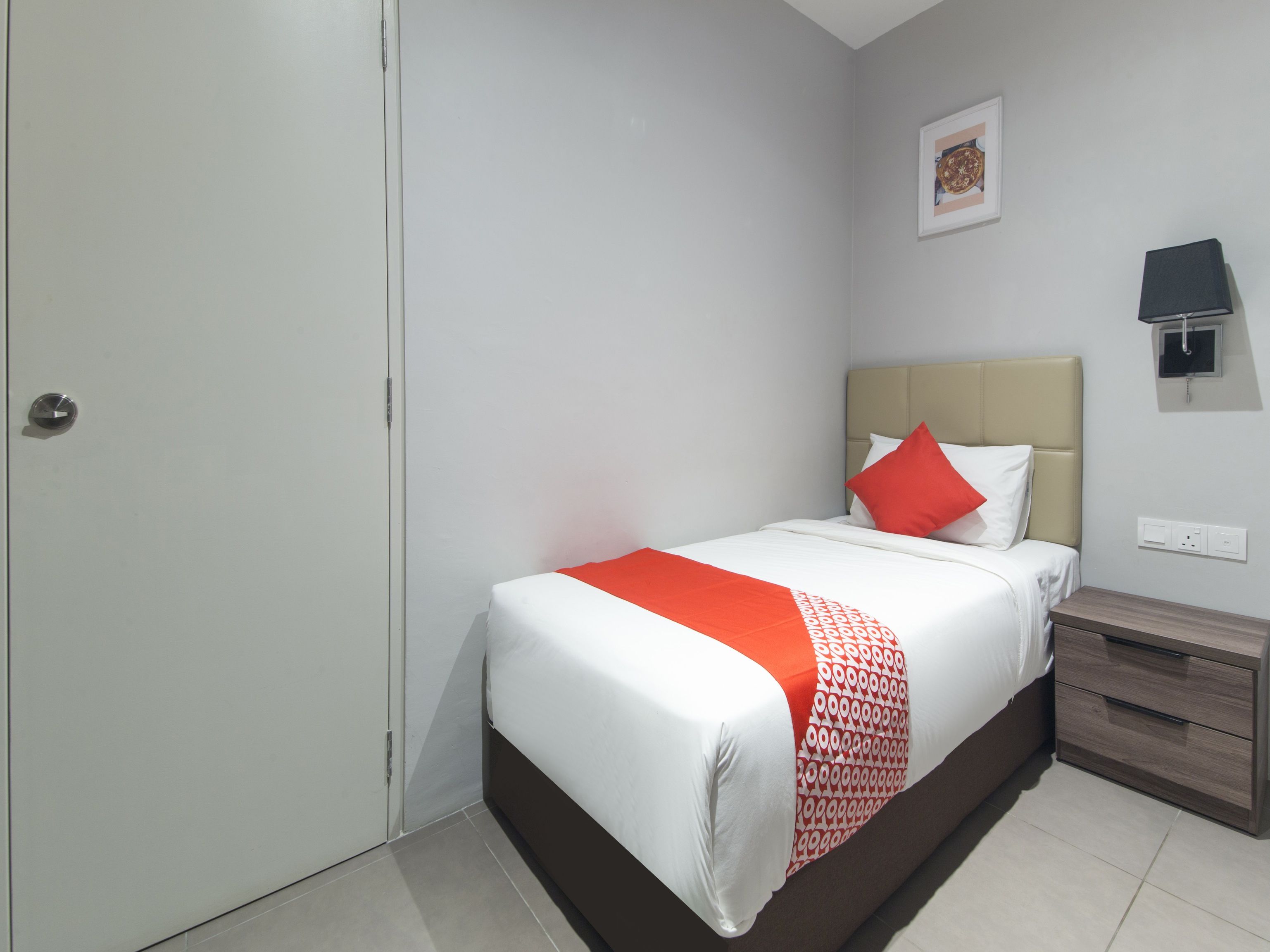 Une chambre à coucher bien rangée, avec un lit, une table de chevet et une lampe fixée au mur.