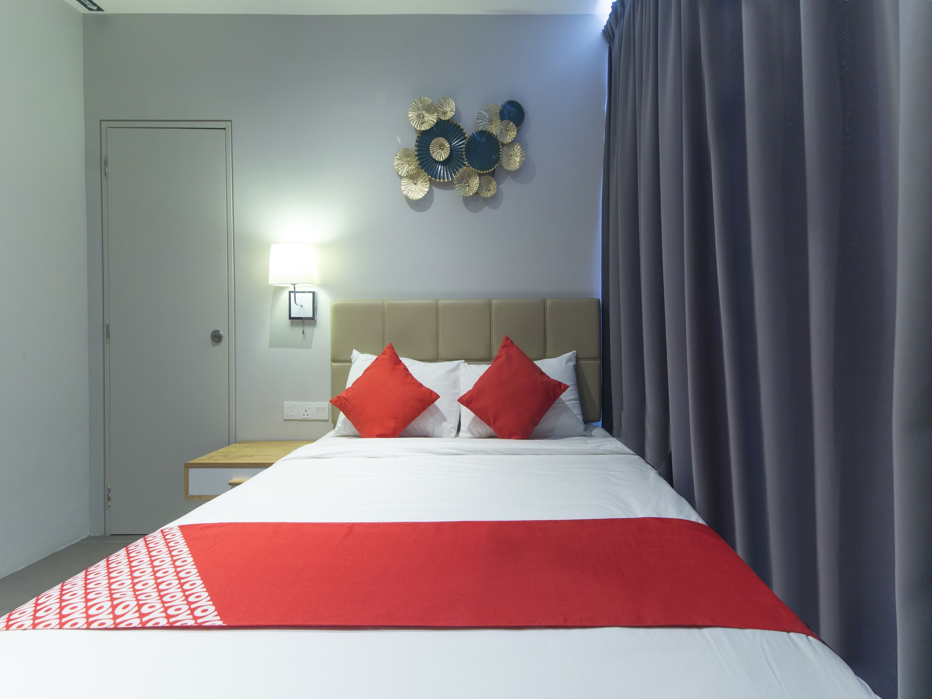Une chambre d’hôtel comprenant un lit, une table de chevet, une lampe fixée au mur et un élément décoratif mural.