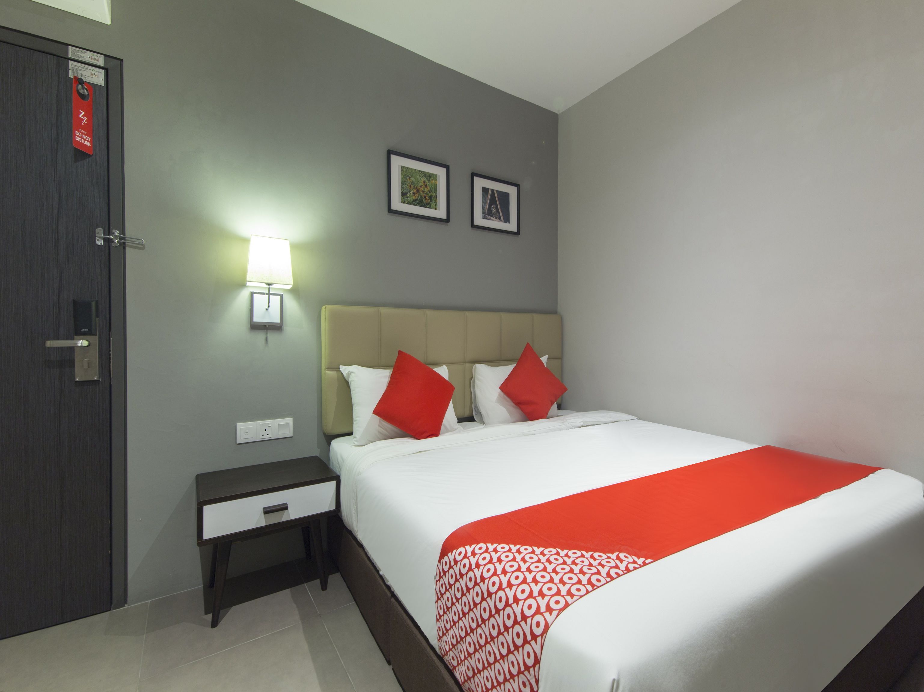 A hotel room with a bed, nightstand, bedside lamp, and a door with a security lock.