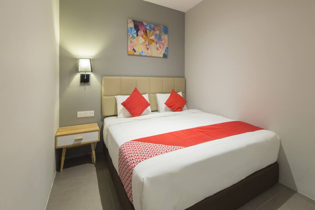 Ein Hotelzimmer mit Bett, Nachttisch, Lampe und einem farbenfrohen, abstrakten Gemälde an der Wand.