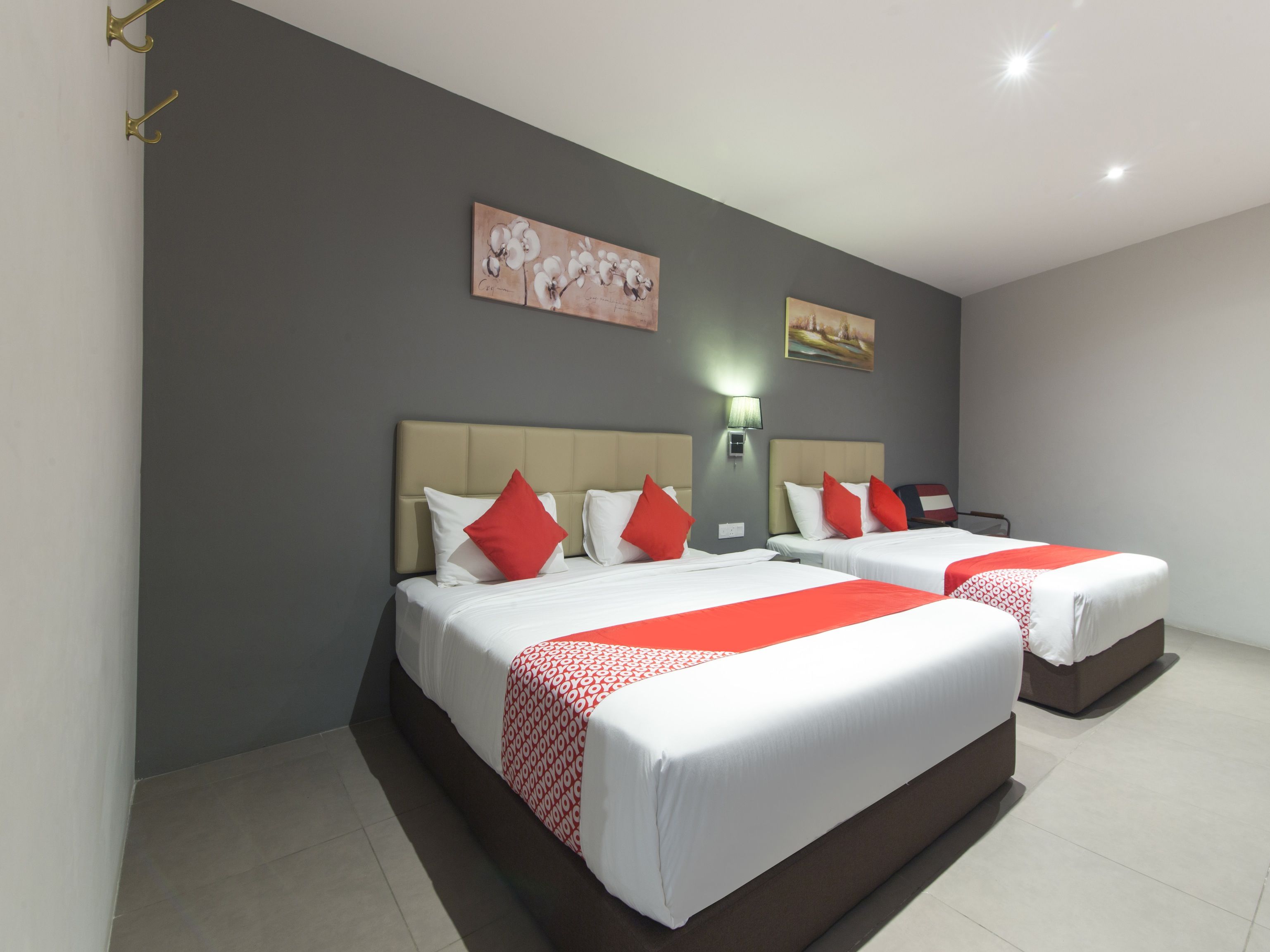 Ein Hotelzimmer mit zwei Betten, jeweils mit weißer Bettwäsche und roten Akzenten, einer grauen Wand und einem Gemälde über den Betten.