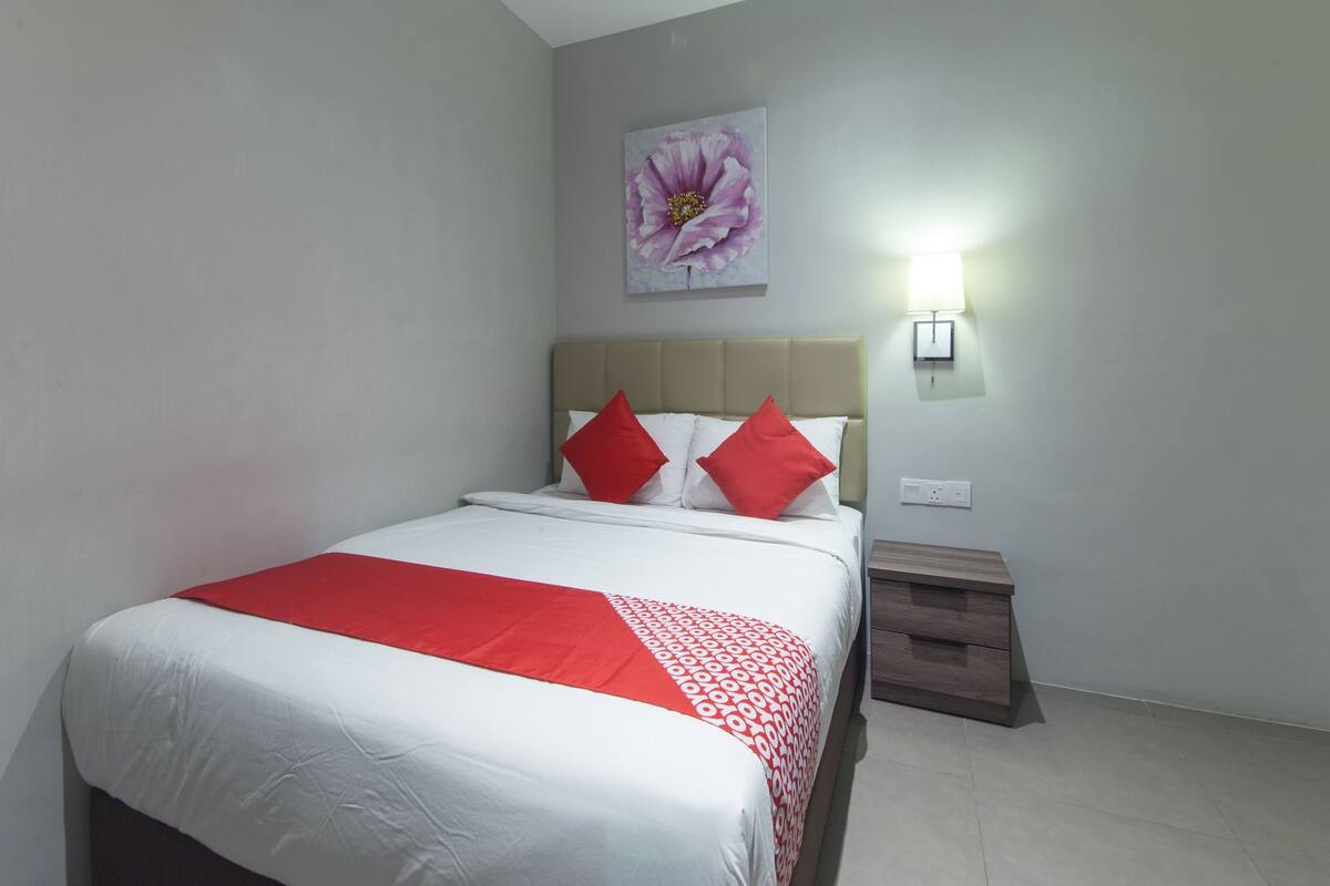 Ein ordentlich eingerichtetes Hotelzimmer mit einem Bett, einem Nachttisch, einer Wandlampe und einem floralen Kunstwerk.