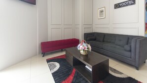 Un salon avec un canapé gris, un banc rouge, une table basse sombre sur laquelle se trouve un panier de fleurs, et une enseigne du Yootel Boutique Hotel accrochée au mur.