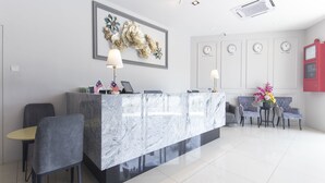 Un espace d’accueil moderne avec un comptoir en marbre, deux drapeaux, un canapé et une horloge indiquant l’heure dans quatre villes différentes.