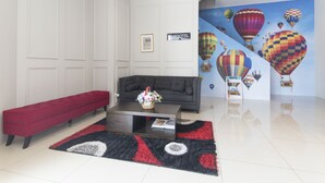 Un hall d’hôtel moderne avec un canapé gris foncé, un banc rouge et une table basse agrémentée d’un arrangement floral. Un grand mur peint représente des montgolfières.