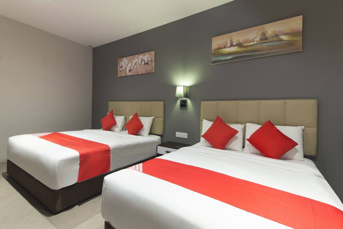 Ein Hotelzimmer mit zwei Betten, jeweils mit weißer Bettwäsche und roten Akzenten, einer grauen Wand und zwei Bildern.