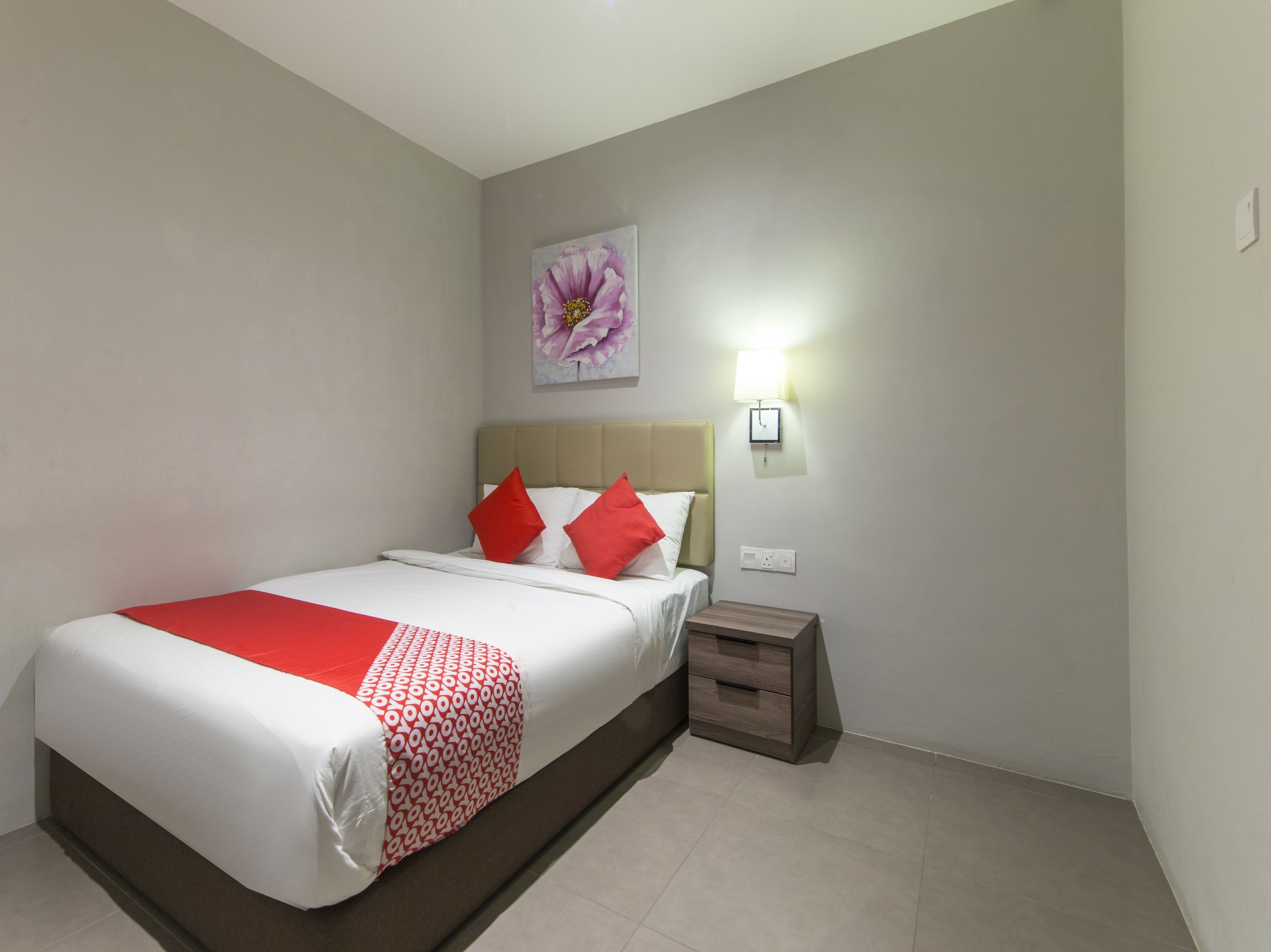 A hotel room with a bed, a nightstand, a wall-mounted lamp, and a painting.