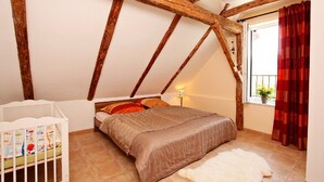 Een slaapkamer met een schuine kap, een bed, een wieg en een raam met gordijnen.