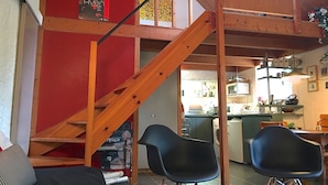 A loft-style living space with a wooden staircase, a kitchen in the background, and a dining area with two black chairs. - MONNA - Maison à Logonna Daoulas - BR4001 (Logonna-Daoulas)