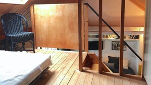 A loft bedroom with a skylight, wooden beams, a bed, a chair, and a staircase leading to a lower level with bookshelves. - MONNA - Maison à Logonna Daoulas - BR4001 (Logonna-Daoulas)