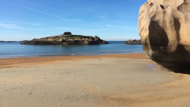 Ein Strand mit einer großen Felsformation und ruhigem Wasser.