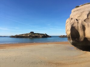 Een strand met een grote rotsformatie en rustig water.
