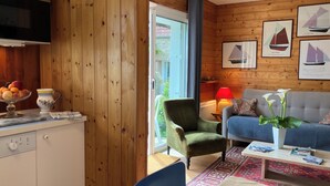 Ein gemütliches Wohnzimmer mit einer Couch, einem grünen Sessel und einem Essbereich mit Tisch für zwei Personen.