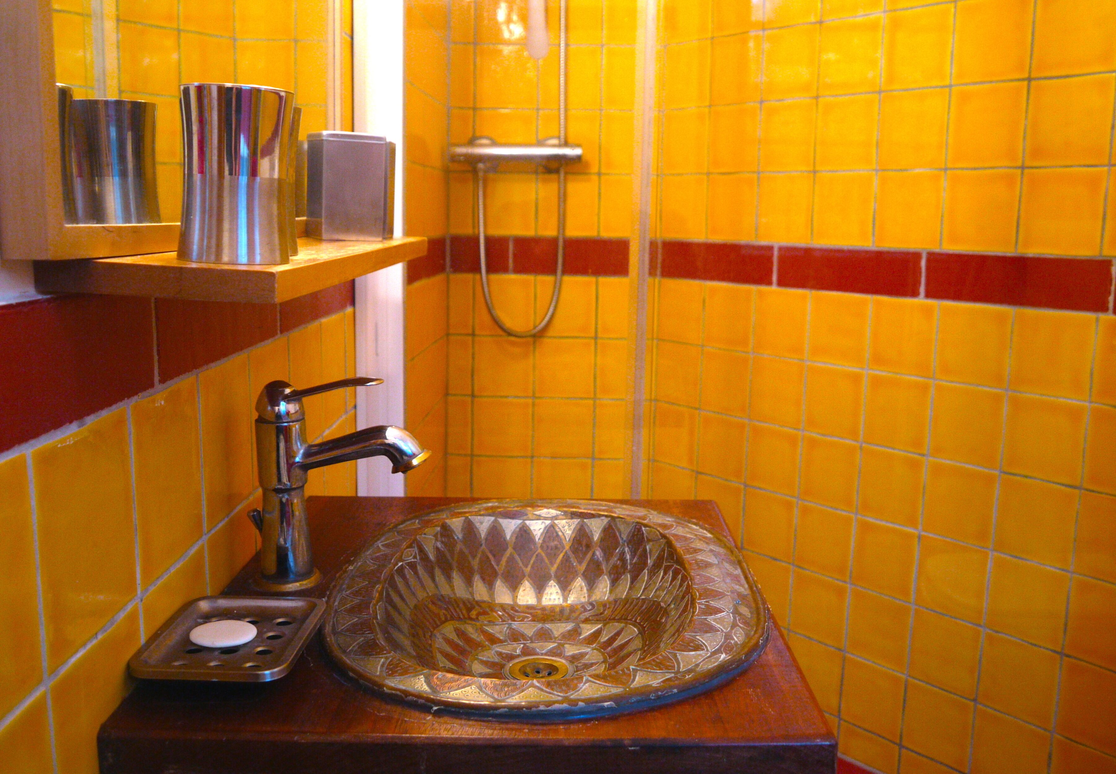 Une salle de bain avec un lavabo en verre, une douchette à main et une étagère contenant des articles de toilette.