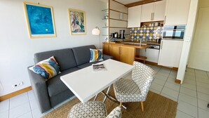 Una cucina moderna con mobili bianchi, un'area pranzo con tavolo bianco e sedie a fantasia e un divano grigio con cuscini colorati.