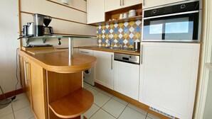 Una cucina compatta con un bancone in legno, mobili bianchi, forno integrato e macchina da caffè.