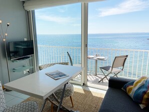 A balcony with a table and chairs, a sofa, and a TV on a glass shelf. - TAL MOR - Apartment with sea view in Carnac, holiday rental pointe Churchill - D11 (Carnac)