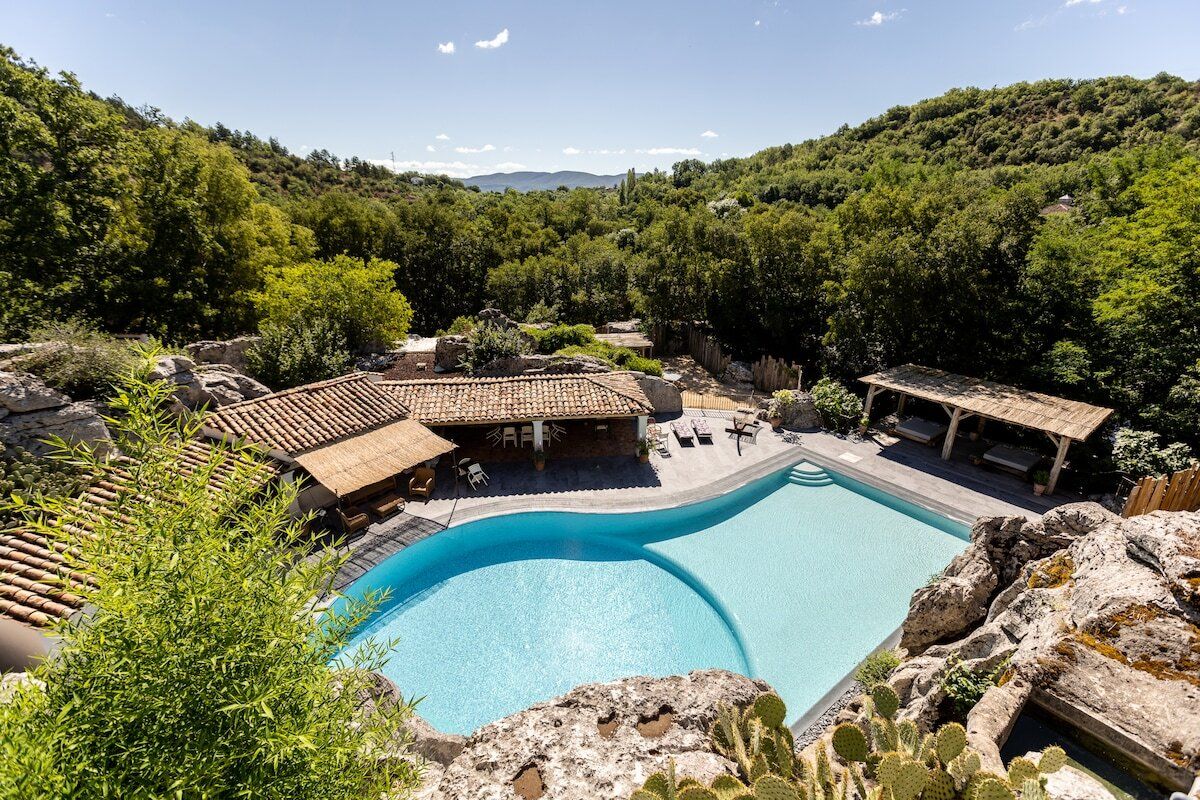 Une piscine au design incurvé, entourée d’une terrasse en bois et d’une structure en pierre.