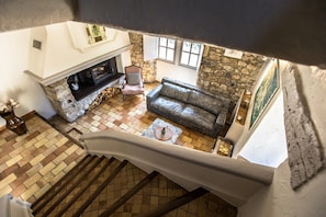 Ein Zimmer mit hohen Decken, einem Kamin, einer Steinwand, einem Holzboden und einem Ledersofa.