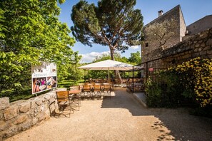 An outdoor dining area with tables and chairs, a sign for a restaurant and pizzeria, and a stone building in the background.
