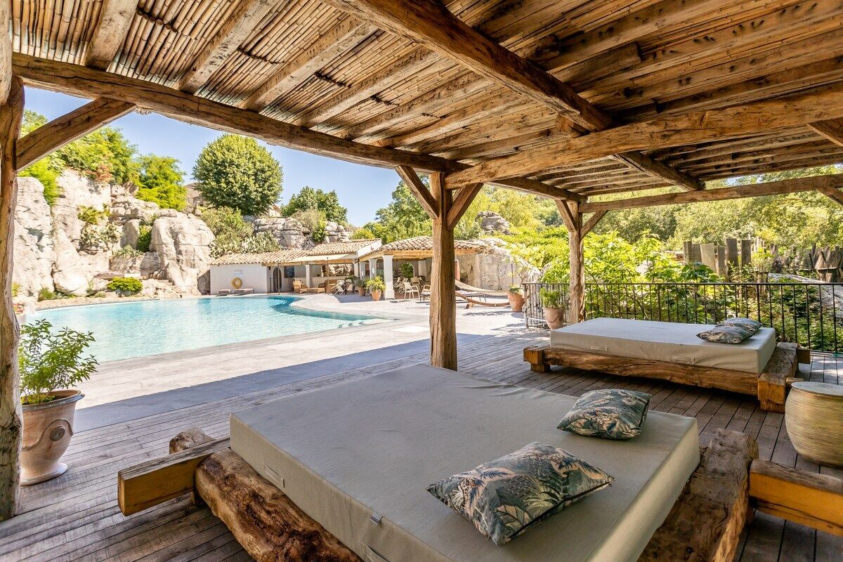 Un espacio al aire libre techado con piscina, terraza de madera y asientos con cojines.