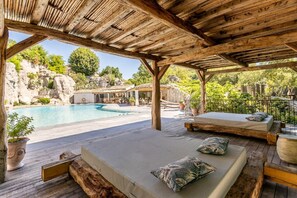 A covered outdoor area with a pool, wooden deck, and seating with cushions.
