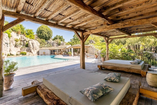 A covered outdoor area with a pool, wooden deck, and seating with cushions. - Gîte Lagon I Terrasse I 4 pers. I Domaine le C4 (Berrias-et-Casteljau)