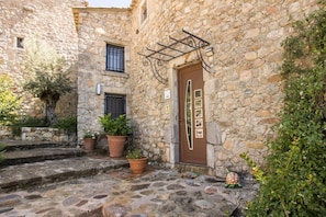 A stone building with a brown door, potted plants, and a small turtle decoration. - Gîte Lagon I Terrasse I 4 pers. I Domaine le C4 (Berrias-et-Casteljau)