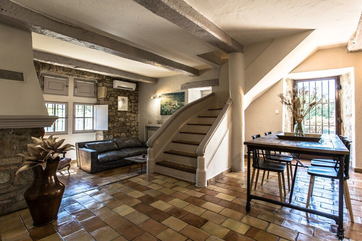 A spacious living area with a stone wall, a staircase, a fireplace, and a dining table.
