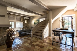 A spacious living area with a stone wall, a staircase, a fireplace, and a dining table.