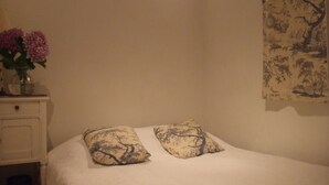 Un dormitori amb un llit, dos coixins, una petita taula de nit amb un ram de flors i un tapet a la paret.
