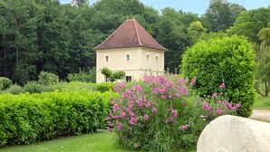 A single-story building with a red-tiled roof, surrounded by lush greenery and flowering plants. - La Tour charming cottage near St Emilion (Lugaignac)