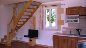 A kitchen with wooden cabinets, a built-in oven, a wooden staircase, and a window with curtains. - La Tour charming cottage near St Emilion (Lugaignac)