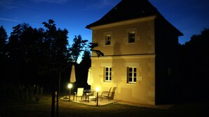 A two-story building with a sloped roof, a patio with outdoor furniture, and a well-lit entrance. - La Tour charming cottage near St Emilion (Lugaignac)