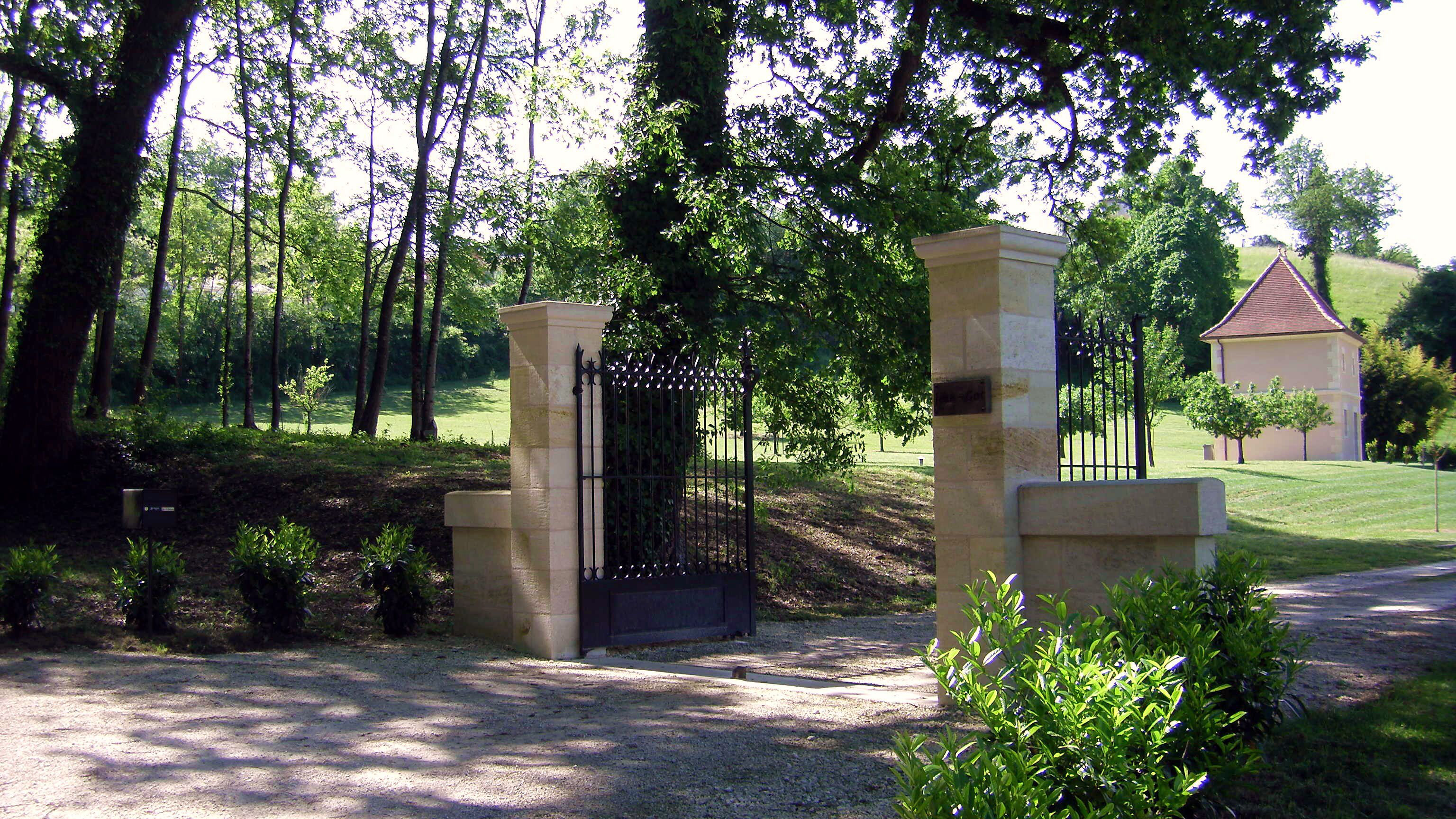 A gated entrance with stone pillars and a metal gate, surrounded by greenery and trees.