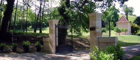 A gated entrance with stone pillars and a metal gate, surrounded by greenery and trees.