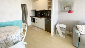 Une cuisine compacte dotée d’appareils électroménagers modernes, un coin repas avec une nappe à pois et un petit espace salon agrémenté d’un coussin à motifs.