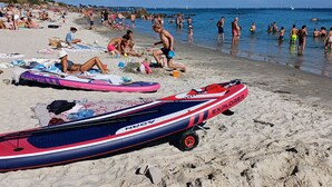 Une plage bondée où les gens se prélassent au soleil et se baignent, et où l’on peut voir plusieurs embarcations gonflables sur l’eau.