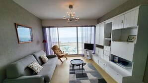 Un salon comprenant un canapé, un fauteuil, un téléviseur et offrant une vue sur la mer grâce à de grandes fenêtres.
