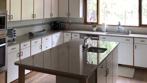 Una cucina moderna con mobili bianchi, un'isola spaziosa con lavandino e vista sull'esterno attraverso una finestra.