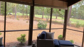 Area salotto esterna coperta con tavolo e sedie, affacciata su un giardino curato con alberi e un campo da golf.