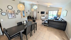 A modern living room with a black sofa, dining table, and chairs, a kitchen area, and a large window. - Stay in a Star Wars-themed vacation home in Emerald Island Resort near Disney. This family-friendly Kissimmee getaway features a private pool and spa, game room, smart-lock check-in, and room for your group to relax after the parks. (Kissimmee)
