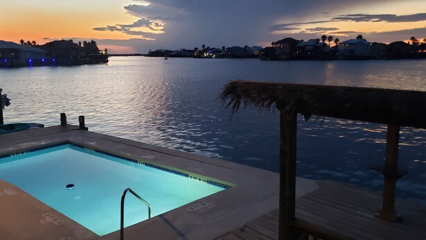 A pool area with a view of a body of water and distant buildings during sunset. - REEL Paradise! <br>*Perfect Couple's Retreat or Big Fun For A Small Family* (Corpus Christi)