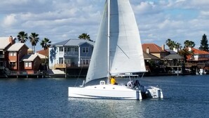 A sailboat on calm water with a backdrop of residential buildings and palm trees. - REEL Paradise! <br>*Perfect Couple's Retreat or Big Fun For A Small Family* (Corpus Christi)