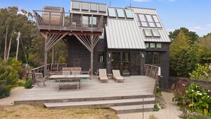 A modern house with a wooden deck, outdoor seating, and a large windowed area. - Country Home in Bolinas (Bolinas)